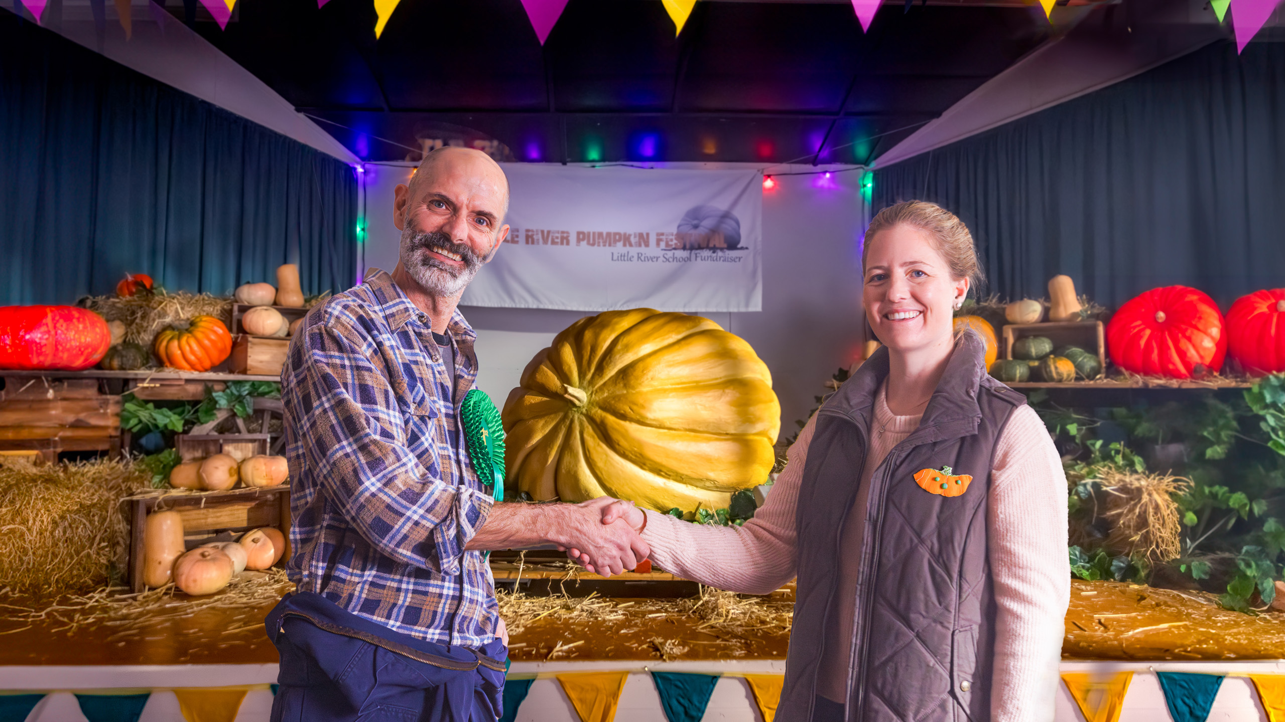two people standing next to a large pumpkin shaking hands